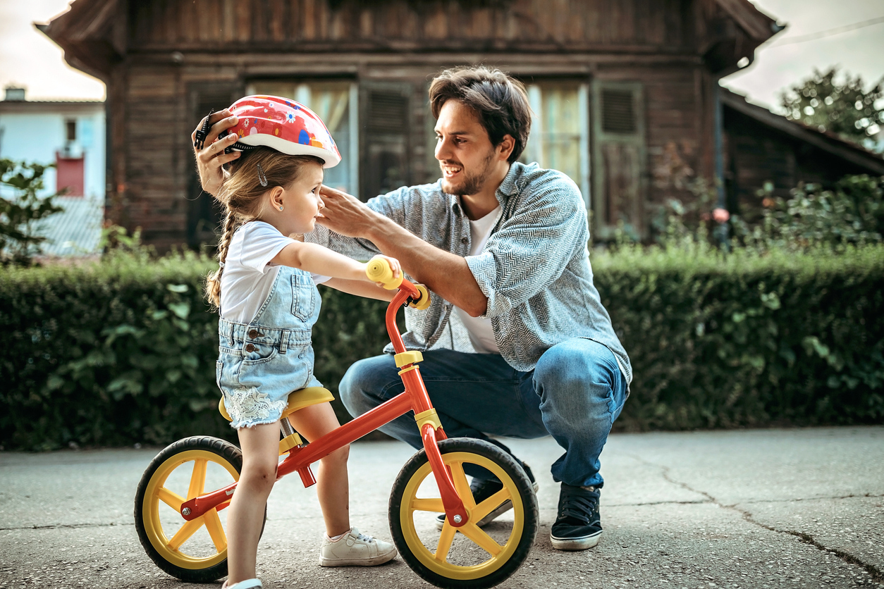 father placing bicycle helmet on daughter